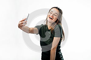 Happy flirting young girl taking pictures of herself through cell phone, over white background