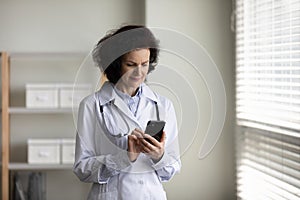 Happy focused 60s mature doctor using cellphone.