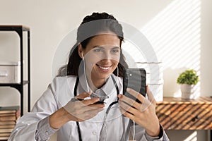 Happy focused female doctor in earphones using mobile phone