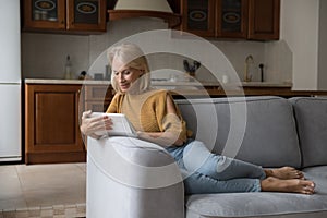 Happy focused mature woman using tablet at home