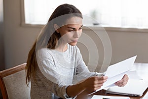 Happy focused young lady reading paper letter with good news.