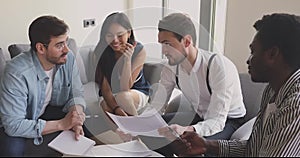 Happy focused young mixed race employees discussing paper reports.