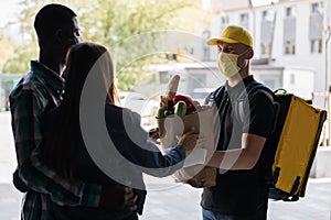 Happy food delivery man with thermal backpack delivers paper bag with fresh vegetables order