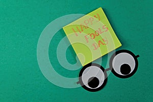 Happy Fools day text on sticky notes with funny faces on green background