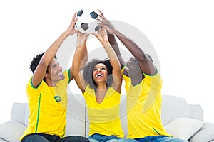 Happy football fans in yellow sitting on couch with ball