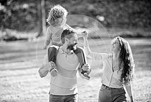 Happy foster family of mother and father carrying adoptive boy child on shoulders, adoption.