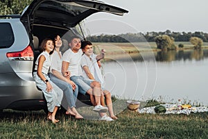 Happy Four Caucasian Members Family Sitting in Trunk of Minivan Car, Mother and Father with Two Teenage Children, Son