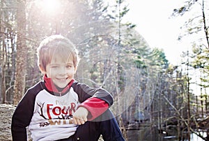 Happy four yearold boy sitting in forest outside photo