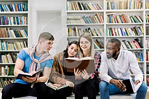 Happy four young university students studying with books in library. Group of multiracial people in college library