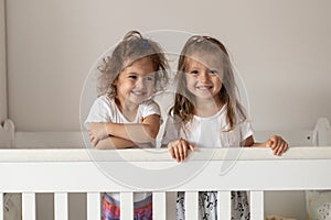 Happy fraternal twins sisters having fun, standing in crib. Happy gitls