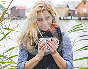 Happy free blonde woman enjoying hot beverages at lakeside.