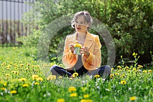 Happy free young woman sitting outdoors on field with flowers and green grass, enjoying spring