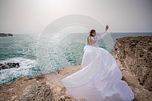 Happy freedom woman on the beach enjoying and posing in white dress. Rear view of a girl in a fluttering white dress in