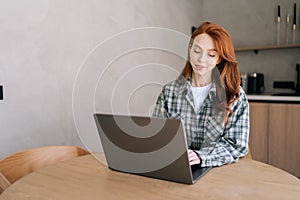 Happy freelancer female sitting at desk, working on computer at home office. Pleasant attractive young woman looking at