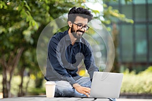 happy freelancer indian man working with laptop pc computer outdoors