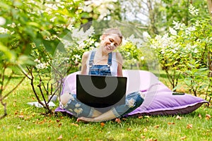 Happy freelancer working in the garden. Writing, surfing in the internet using laptop. Young woman relaxing and having