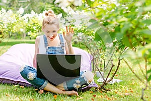 Happy freelancer working in the garden. Writing, surfing in the internet. Young woman waving to the camera during a