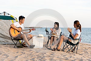 Happy friend have fun playing guitar and clap in camp they smiling together in holiday on sand beach near camping tent