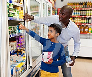 Happy friendly African family of father and tween son shopping together in supermarket