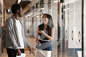 Happy friendly diverse colleagues talking laughing walking in office hallway