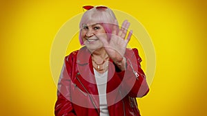 Happy friendly elderly woman waves hand palm in hello gesture welcomes someone positive emotions