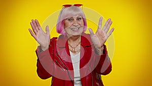 Happy friendly elderly woman waves hand palm in hello gesture welcomes someone positive emotions