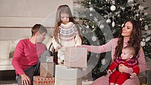 Happy friendly family is folding gifts under big Christmas tree