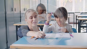 Happy friendly school teacher and pupil girl at desk