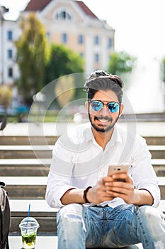 Happy and friendly young indian man using or Working on Smart Phone and sitting outdoor Stair. Social communicate technology in Bu