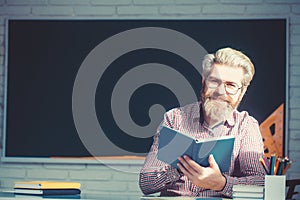 Happy friendly young teacher or post graduate male student standing holding book in front of a blank chalkboard.