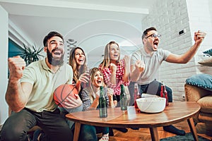 Happy friends or basketball fans watching basketball game on tv