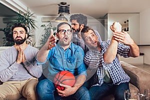 Happy friends or basketball fans watching basketball game on tv and celebrating victory at home.