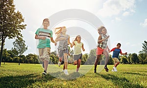 Happy friends, children and running with grass field in nature for fun, playful day or sunshine at park. Diversity or