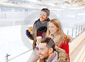 Happy friends with coffee cups on skating rink