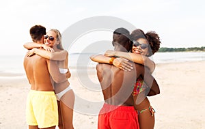 Happy friends or couples hugging on summer beach