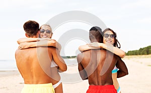 Happy friends or couples hugging on summer beach