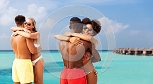 Happy friends or couples hugging on summer beach