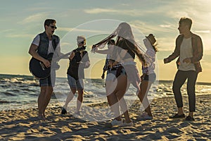 Happy friends dancing on the beach. Men is playing guitar