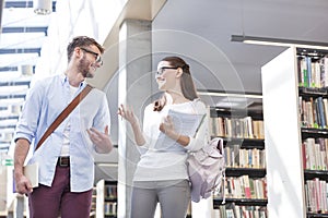 Happy friends discussing over books by library at university