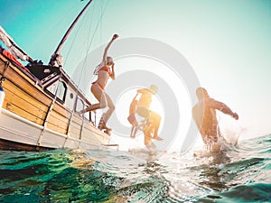 Happy friends diving from sailing boat into the sea - Young people jumping inside ocean in summer excursion day - Vacation, youth