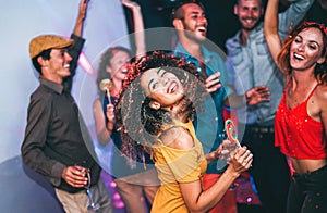Happy friends doing party at night club - Young woman having fun with her group of mates eating candy lollipops inside disco