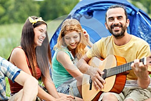 Happy friends with drinks and guitar at camping