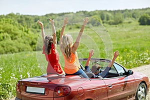 Happy friends driving in cabriolet car at country