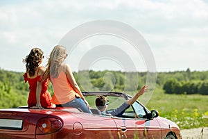 Happy friends driving in cabriolet car at country