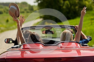 Happy friends driving in cabriolet car at country