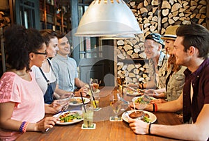 Happy friends eating and drinking at bar or pub