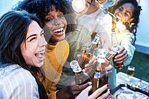 Happy friends enjoying party on rooftop terrace - Group of multiracial young people drinking beer bottle at brewery pub garden -