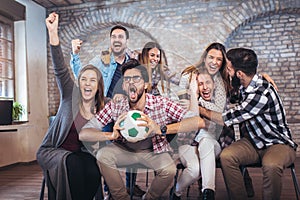 Happy friends or football fans watching soccer on tv and celebrating victory