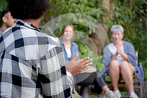 Happy friends group doing recreation with man playing guitar and friends and children singing at camping.