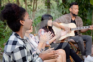 Happy friends group doing recreation with man playing guitar and friends and children singing at camping together.